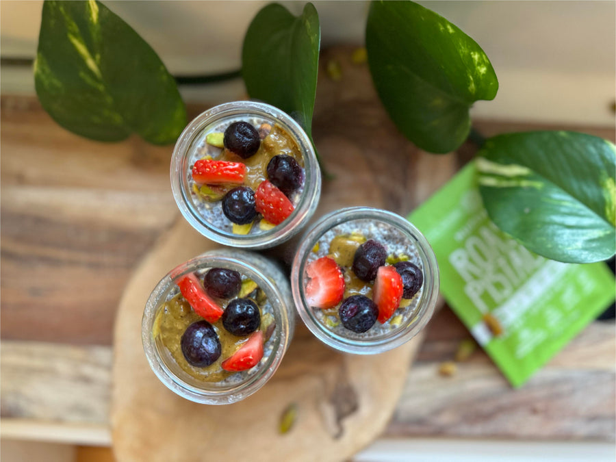 Pistachio butter chia pudding topped with strawberries, blueberries, and raspberries in glass jars