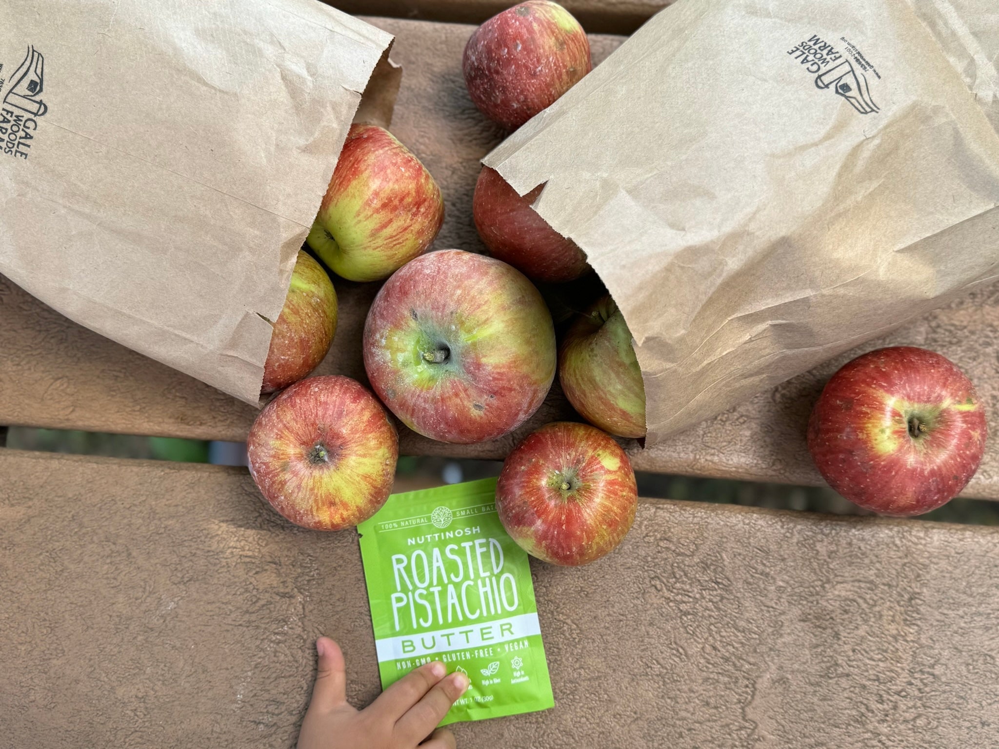 Nuttinosh roasted pistachio butter packet with fresh apples and paper grocery bags on a wooden table