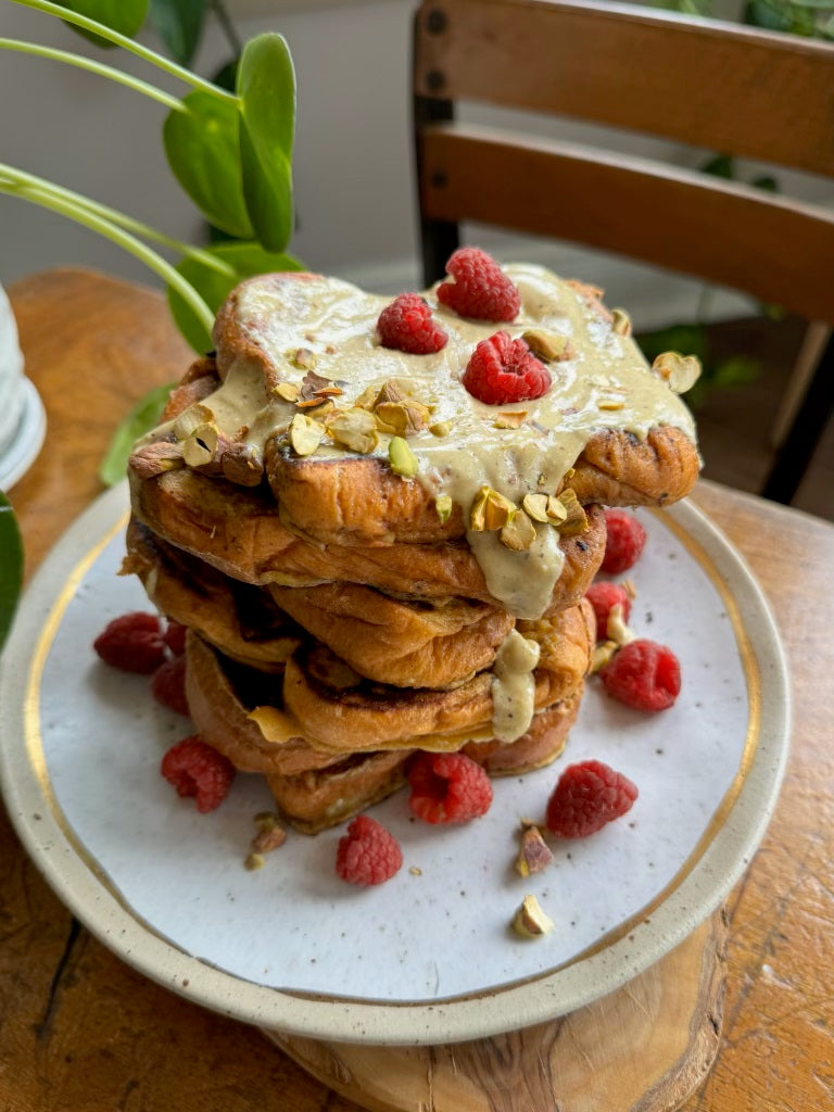 Stack of waffles topped with pistachio butter, raspberries, and chopped pistachios on a plate