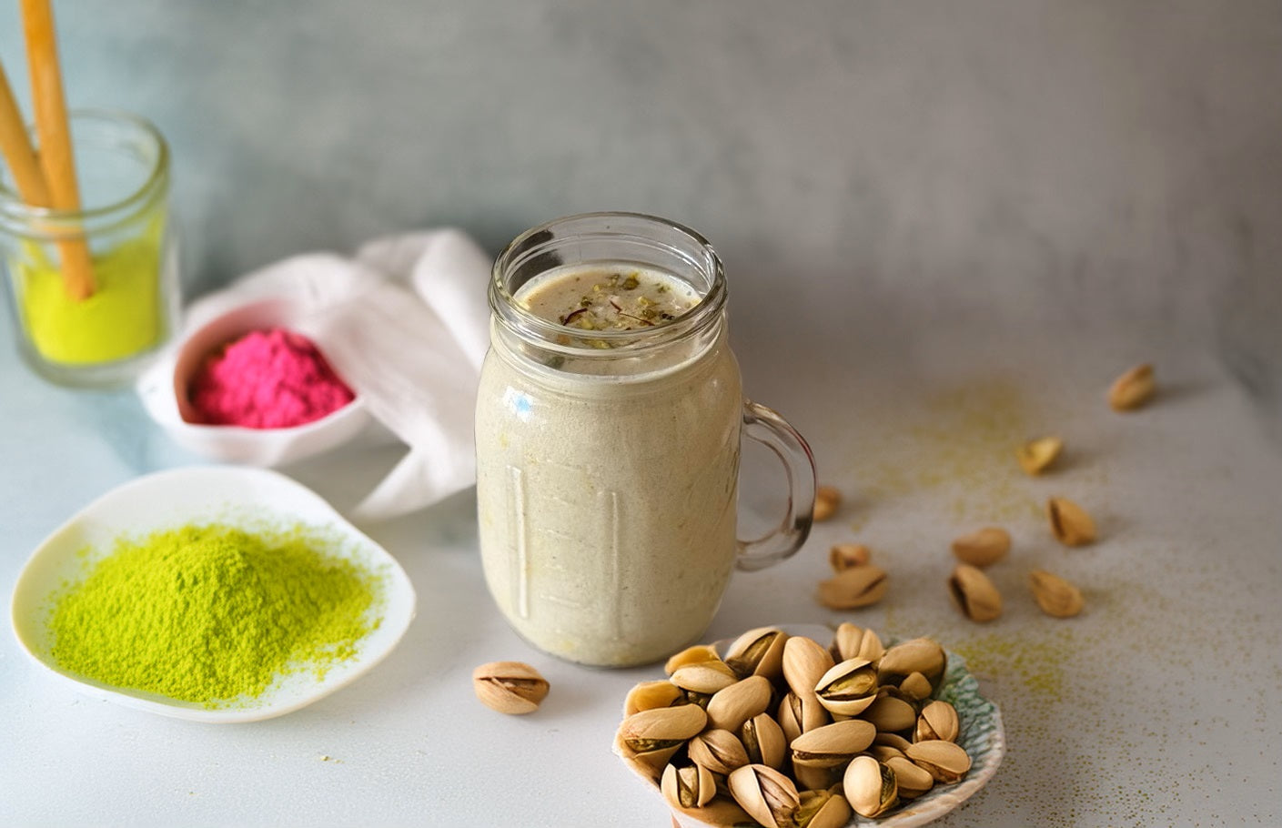 Creamy pistachio smoothie in a glass jar with pistachios and pistachio powder on the side