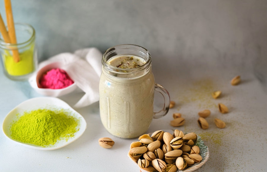 Creamy pistachio smoothie in a glass jar with pistachios and pistachio powder on the side