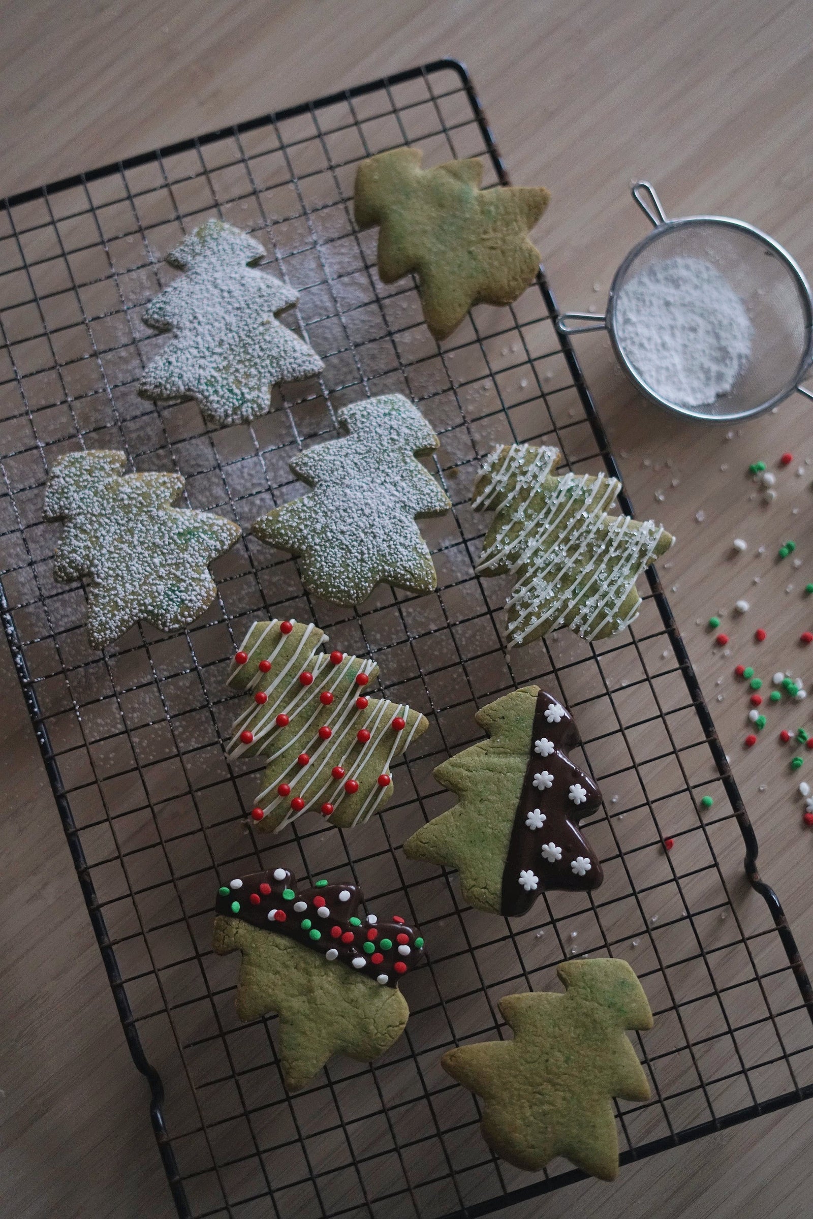 Christmas tree–shaped cookies decorated with icing and sprinkles on a cooling rack