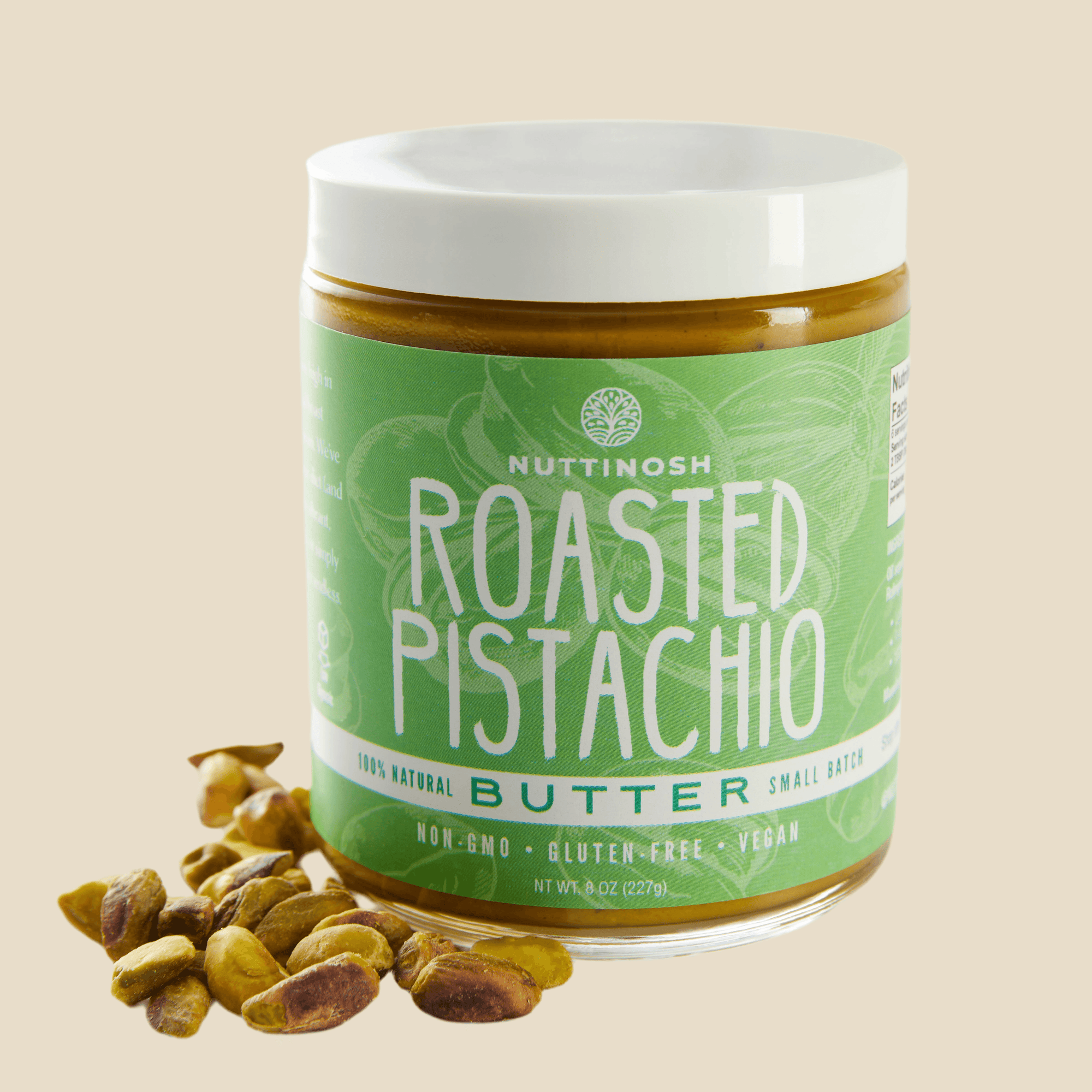 Jar of Nuttinosh roasted pistachio butter with green label and white lid, placed next to pistachios.
