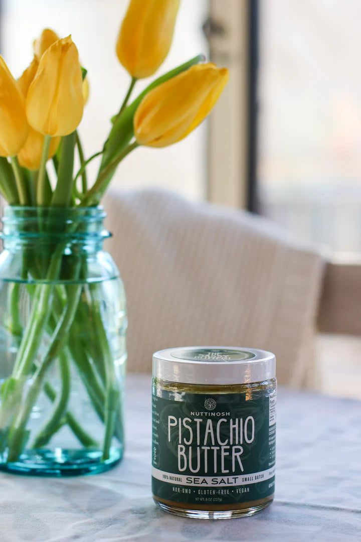 Jar of Nuttinosh pistachio butter with sea salt placed on a table next to a vase of yellow tulips